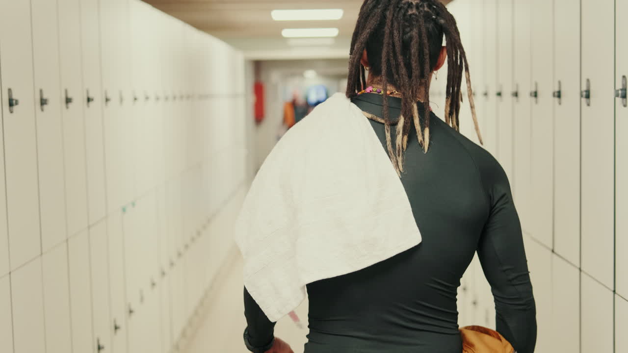 Person with Dreadlocks Walking Through a Modern Locker Room