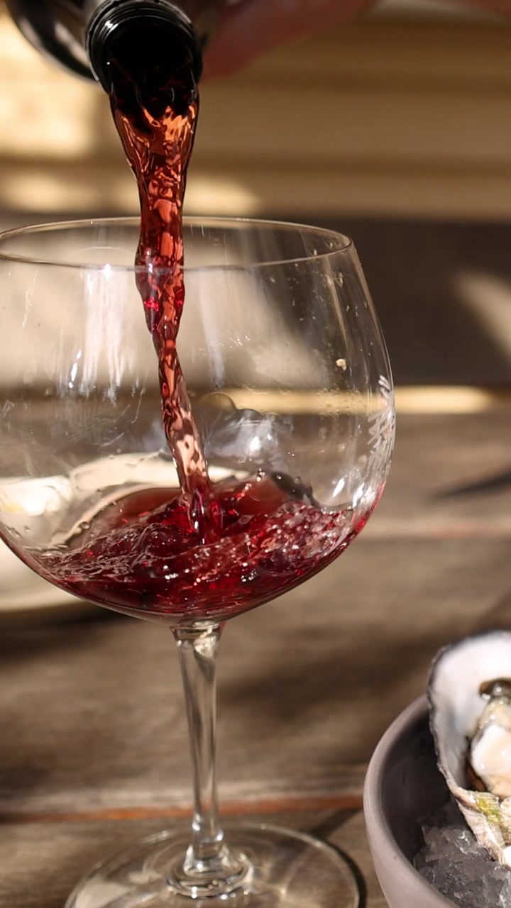 Un filo di vino rosso viene versato in un calice di vetro su un tavolo all'aperto e soleggiato.
