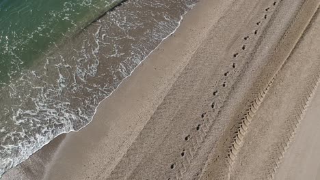 Aerial-views-over-a-beach-with-gentle-waves-and-people-walking-along-the-shore-calmly