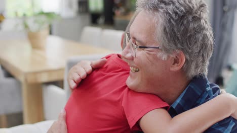 feliz abuelo caucásico y nieto sentado en el sofá y abrazando, cámara lenta