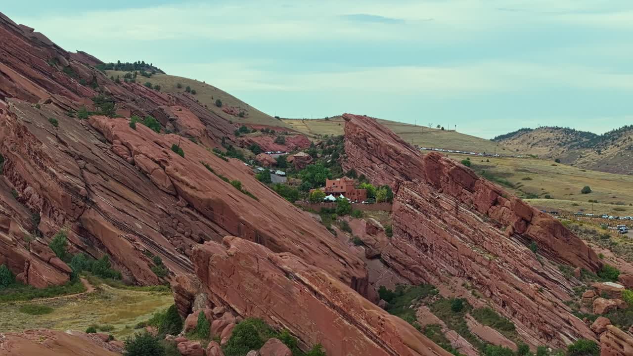 Drone aerial tracking left over Red Rocks Amphitheatre showing vast red cliffs and winding trails in rugged terrain