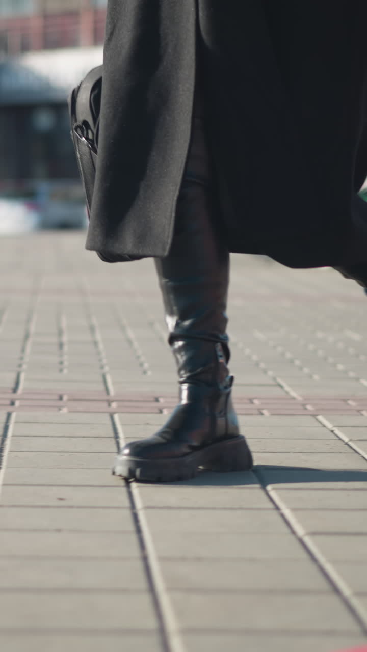 vista lateral de la pierna de un individuo con abrigo negro y pantalón de red, caminando a toda velocidad a través de un camino entrelazado, con una bicicleta verde estacionada y edificios urbanos borrosos en el fondo