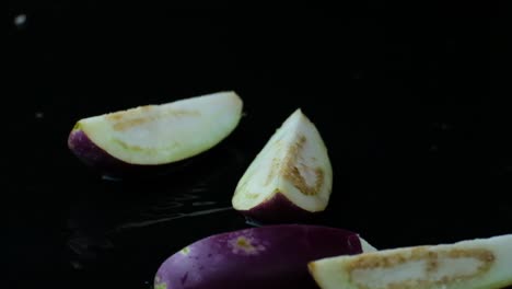in quarters sliced aubergines falling down into clean puddle with black studio background