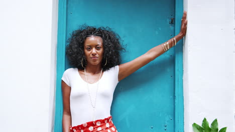 joven negra a la moda con pantalones de punto rojo inclinándose en una puerta mirando a la cámara