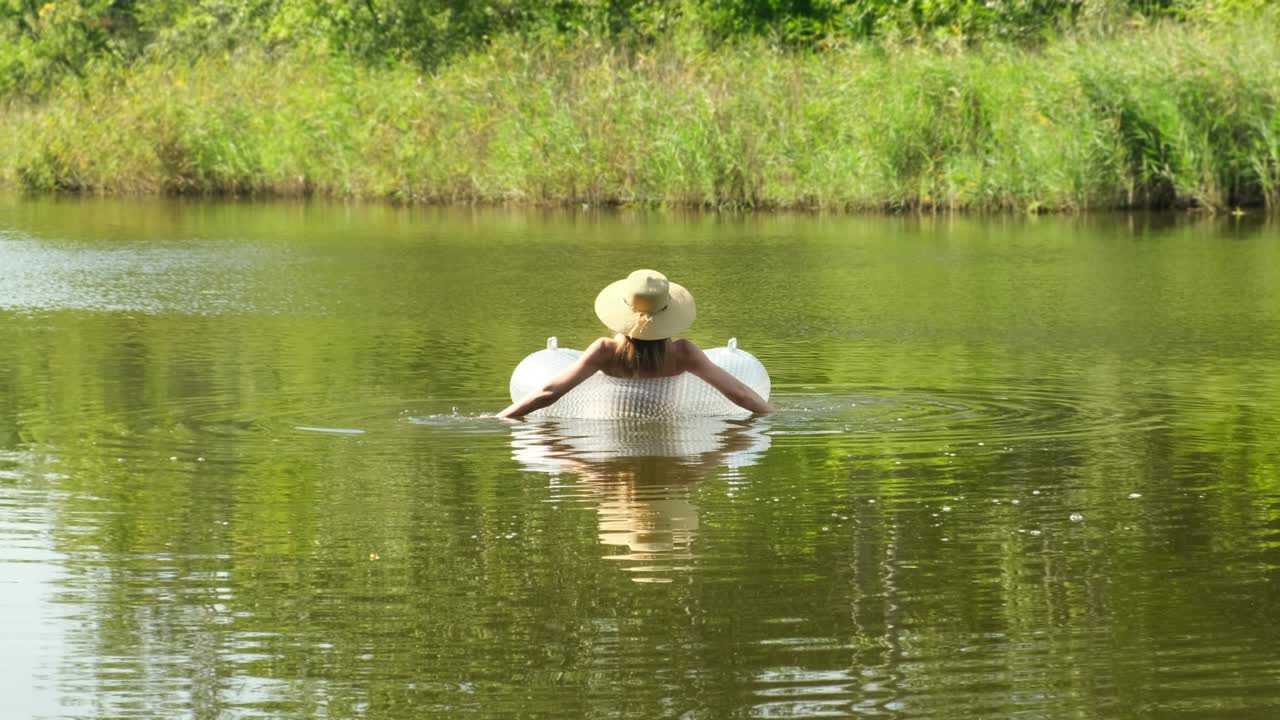 mujer en traje de baño y sombrero de paja está flotando con un círculo inflable en el estanque del lago río. la chica descansa en el anillo de natación en una piscina con agua azul. concepto de viaje, vacaciones, fines de semana, vacaciones, relajarse en la naturaleza, descanso, relajación