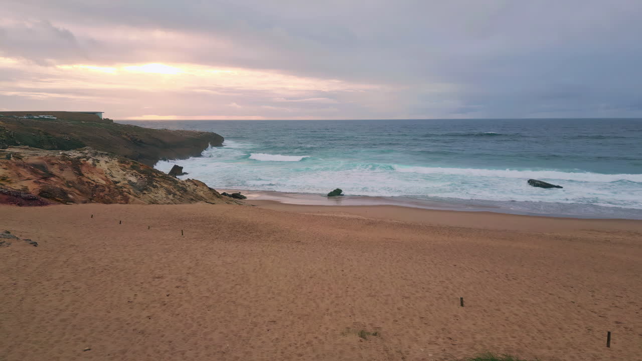 Coastal landscape lit sunset light with ocean waves gently washing sandy beach.