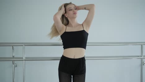 fit girl in black clothes performing contemporary. female dancer shows flowing motions, body and hands waves at white room. modern ballet dance choreography. young woman is moving smoothly