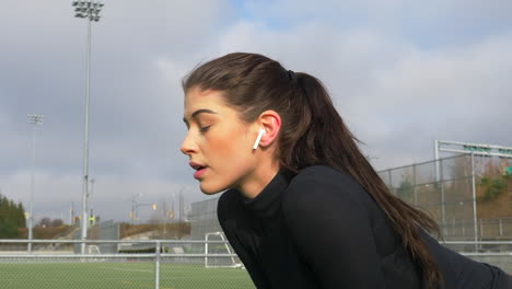 beautiful tired woman bending forward with hands on knees and breathing while taking a rest after running around the soccer field