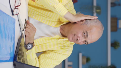 Vertical-video-of-Home-office-worker-old-man-looks-at-camera-with-happy-and-smiling-face.