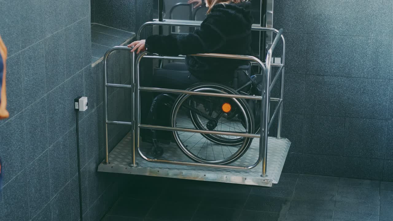 Woman with disabilities in a wheelchair climbs stairs on a mechanical lift.