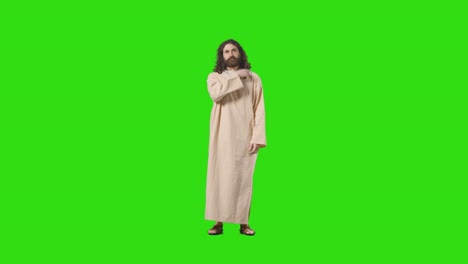 studio shot of man wearing robes and sandals with long hair and beard representing figure of jesus christ praying on green screen 1