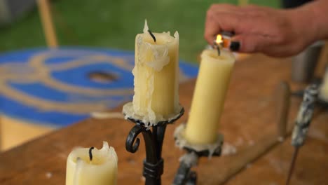 Old-used-candles-with-melted-wax-on-rustic-black-candlestick-placed-on-table,-hand-with-black-nails-lights-them