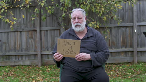 a homeless man in a park holding a i want a job card