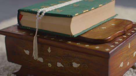 close up of closed copy of the quran on stand at home with prayer beads