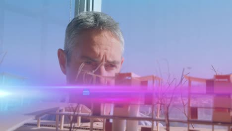 animation of pink light beams and lens flare over male architect looking at architectural model