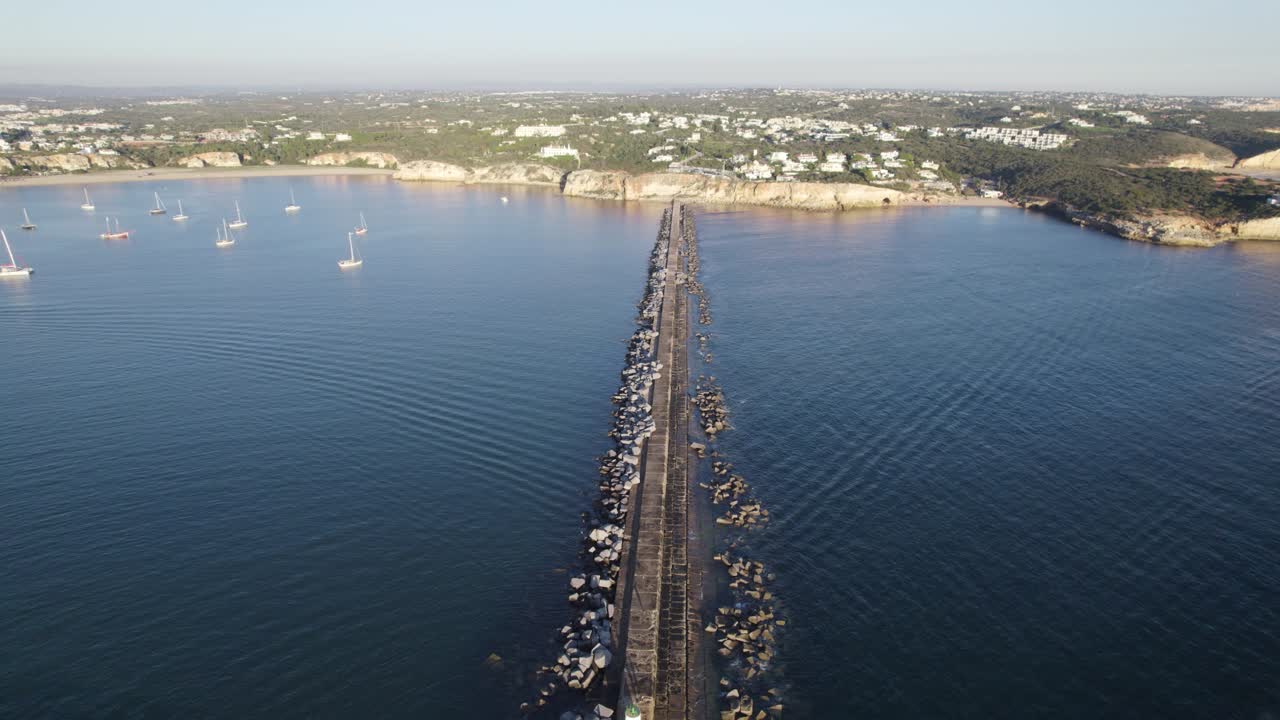 Aerial pullback over Ferragudo Breakwater with sailing boats moored near coastline, Portim&atilde;o
