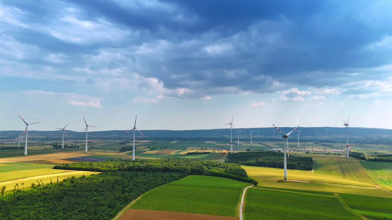 Striking green summer fields with wind farms. Drone flight over the countryside on cloudy day