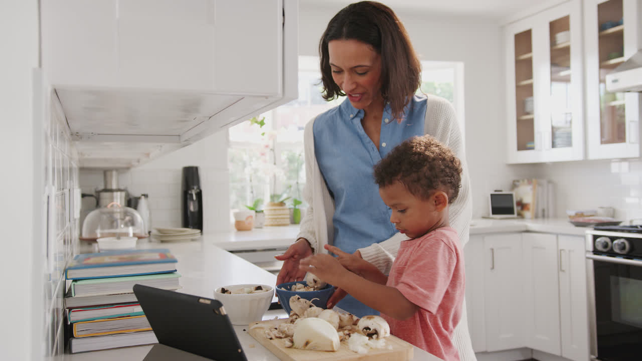 madre milenaria y hijo pequeño preparando comida juntos en la cocina, vista lateral