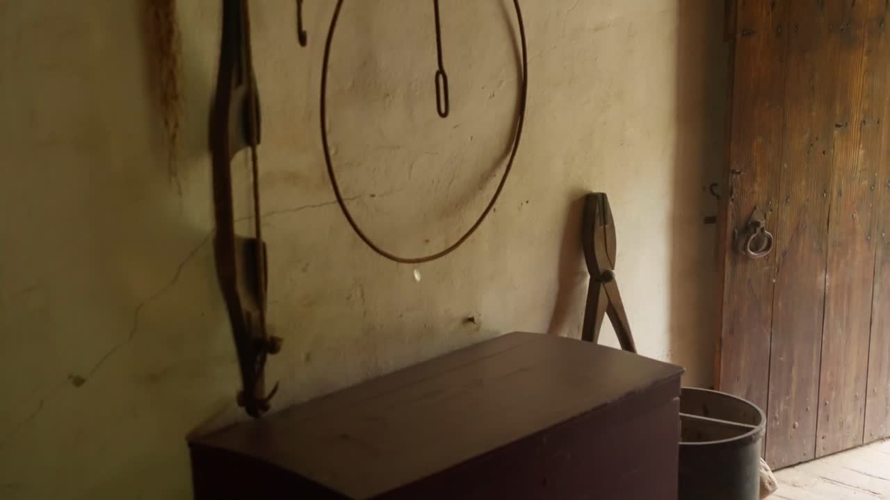 Rustic interior of historical farmhouse showing wooden chest hanging metal tools and weathered walls. Traditional dutch agricultural storage room with wooden door at open air museum exhibit