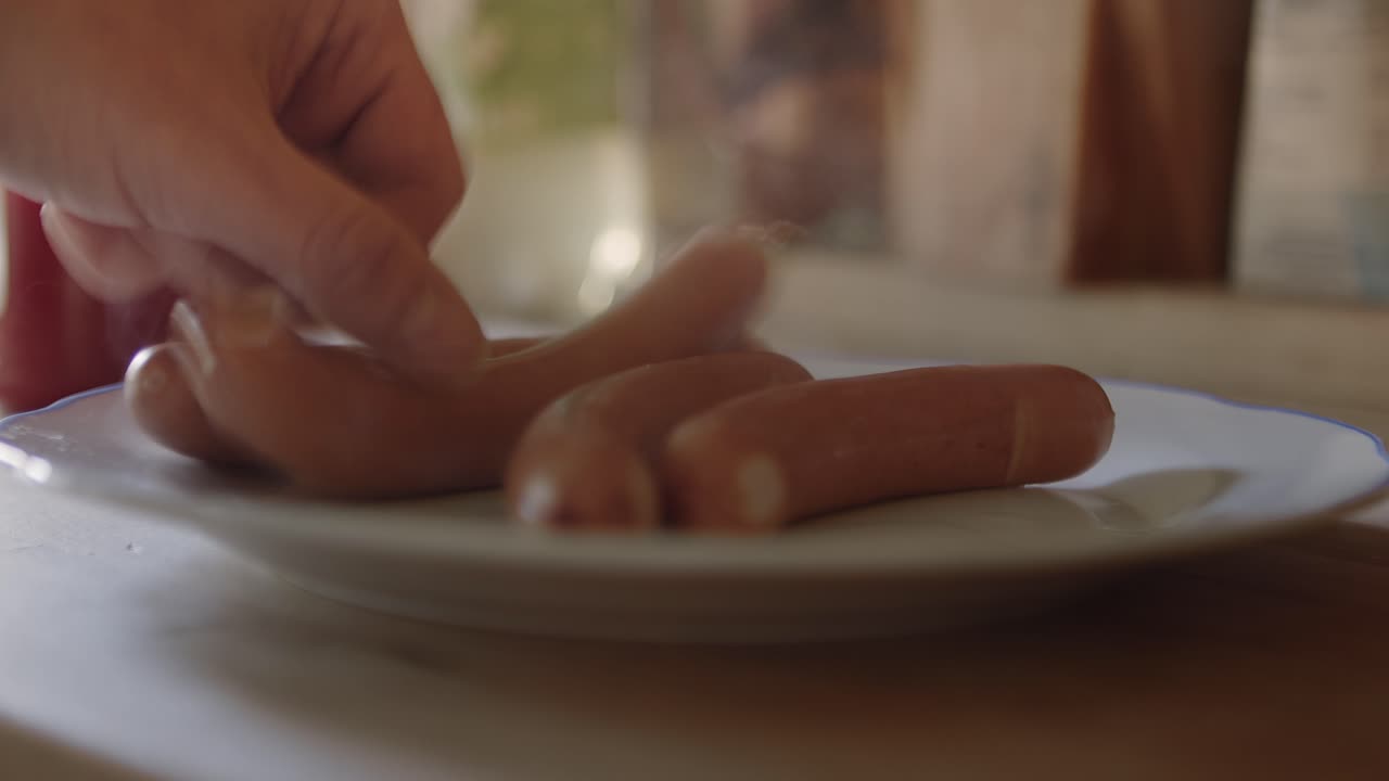 una mano arroja salchichas calientes humeantes en un plato y las alinea
