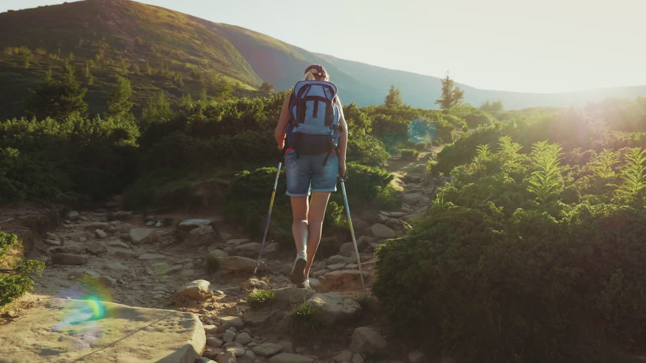 una turista con una mochila con bastones de trekking sube por el camino de la montaña en los rayos del s