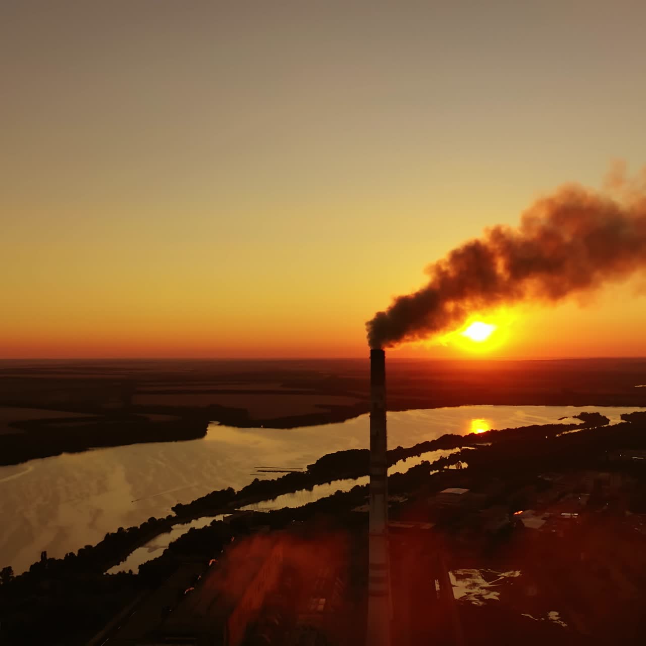 Smoke from industrial pipe against the sunset. Factory near the river on the setting sun. Pollution the atmosphere.