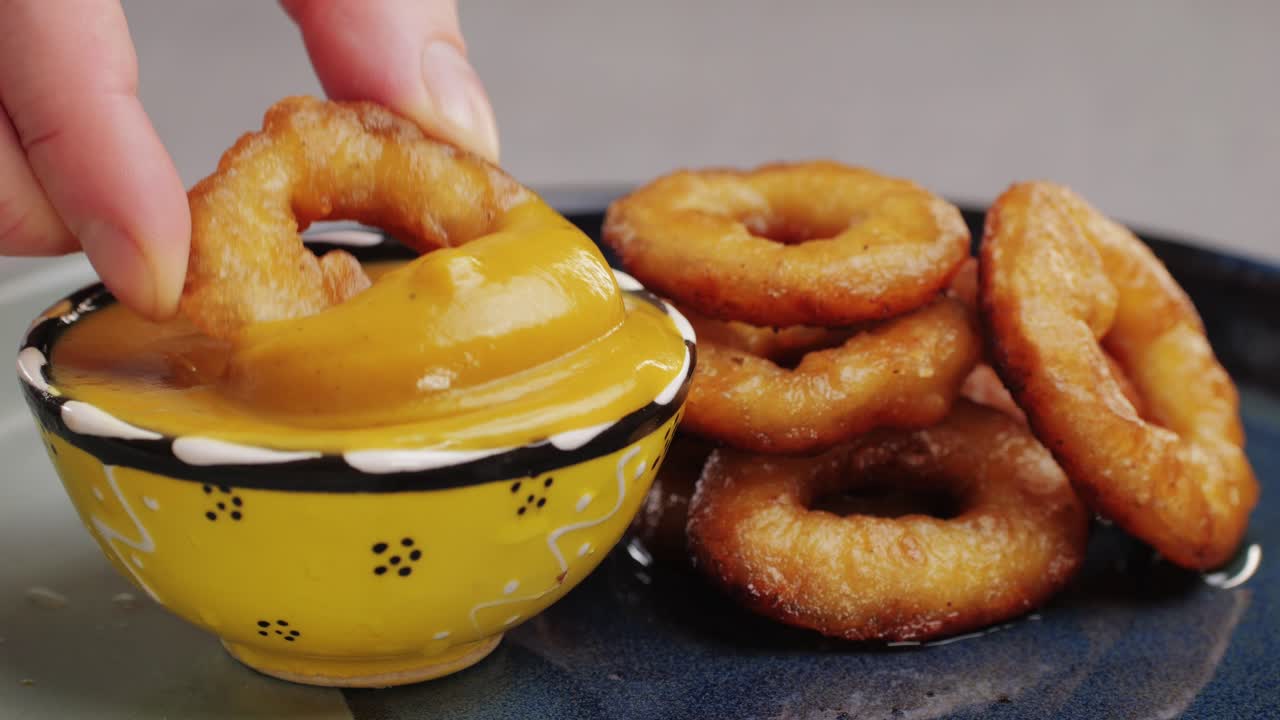 Fried crispy onion rings dipping in chimichuri sauce close-up macro. Roasted onion rings for snacks at bar, cafe. Fast food. Delivery. Beer snacks