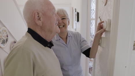 caregiver assisting elderly man with thermostat