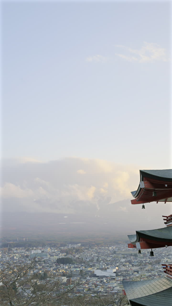 Chureito Pagoda stands tall, overlooking a sprawling Fujikawaguchiko city as the sun sets behind majestic Fuji mountain. Vertical video