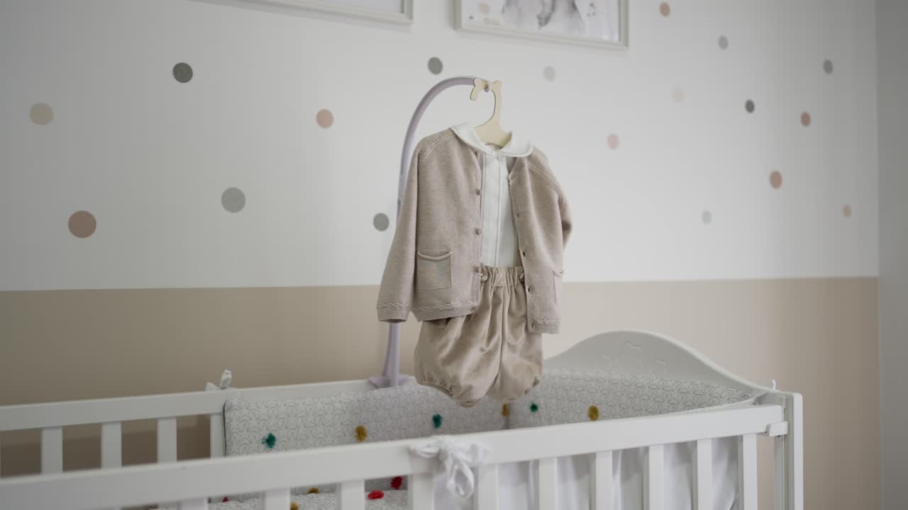 Adult hand shows baby onesie above white crib in softly lit nursery interior