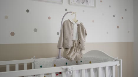 adult hand shows baby onesie above white crib in softly lit nursery interior