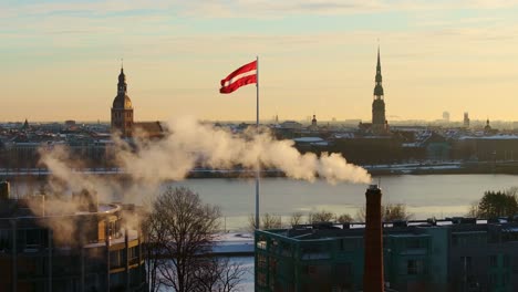slow-motion shot of latvia’s flag waving at sunrise, historic riga in background