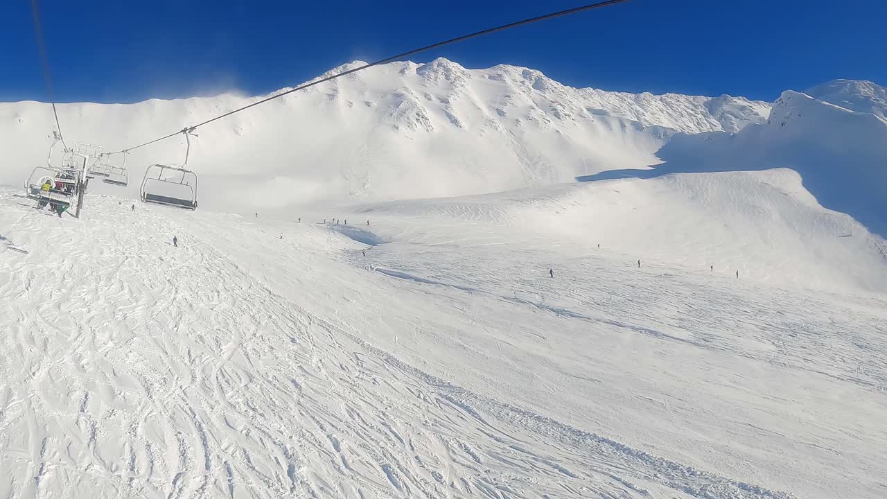 Salita in seggiovia (POV): vista di sciatori che scendono in una giornata di sole