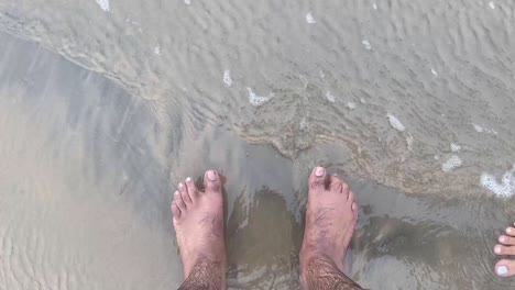 water sliding down the feet of an indian man standing on the beach