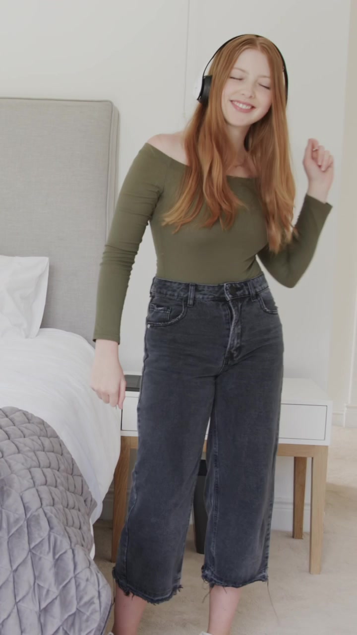 Woman putting on headphones, swaying and adjusting, then sitting and lying on bed relaxing to music