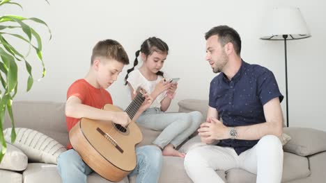 young son playing guitar for dad sitting on couch. happy family spending time together. 4k vifeo