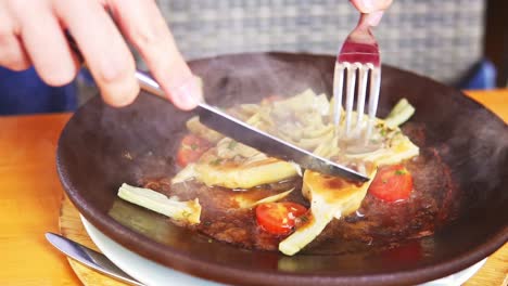 close up shot of person using knife and fork frying food with tomato, homemade