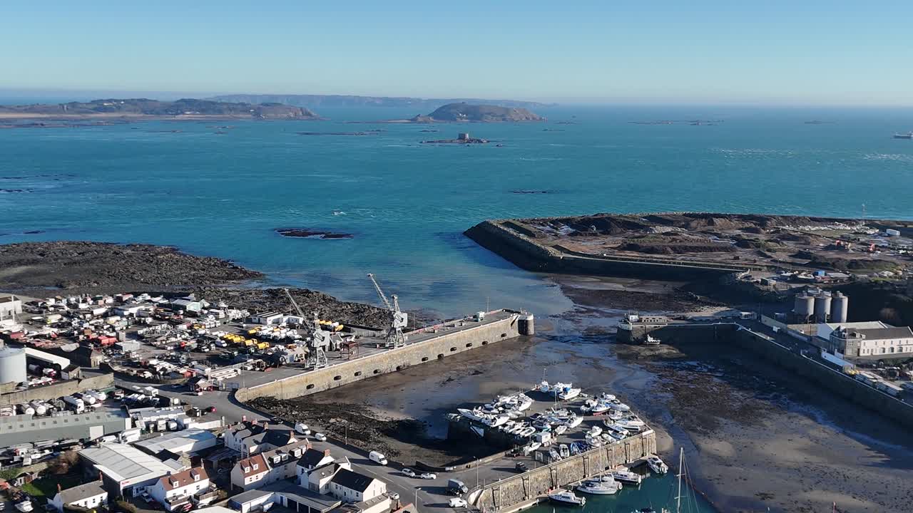 Guernsey St Sampsons harbour.Slow circling drone footage of harbour entrance and marina at low tide over industrial zone with final views of Herm and Jethou in late afternoon sun