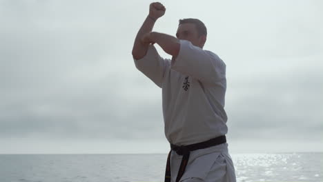 Atleta-Enfocado-Ejercitando-Karate-En-Primer-Plano-De-La-Playa.-Hombre-Entrenando-Habilidades-De-Lucha