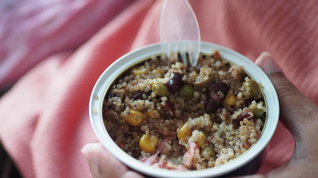close up de una persona comiendo una lata de quinoa con verduras y frijoles