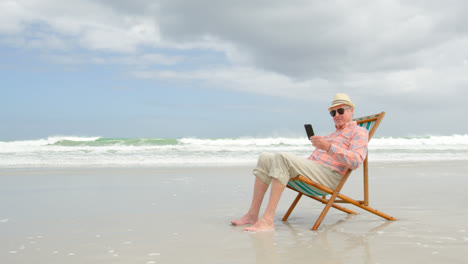 vista lateral de un anciano caucásico usando un teléfono móvil en la playa 4k