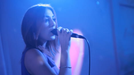 woman singing on dark stage. young pretty woman singing in microphone on dark stage