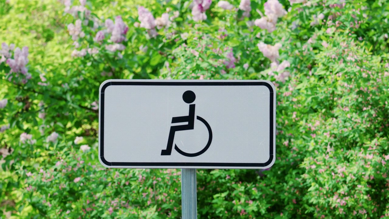 Wheelchair accessibility sign displayed outdoors against a background of green plants and flowers