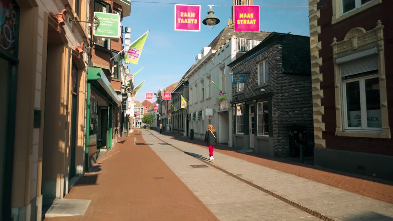 Dolly shot moves right, revealing an empty Maasstraat in Weert, Limburg, as a lone woman walks through the quiet shopping street. Architecture and serene atmosphere in Weert, Limburg, Netherlands