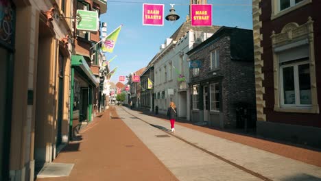 dolly shot moves right, revealing an empty maasstraat in weert, limburg, as a lone woman walks through the quiet shopping street. architecture and serene atmosphere in weert, limburg, netherlands