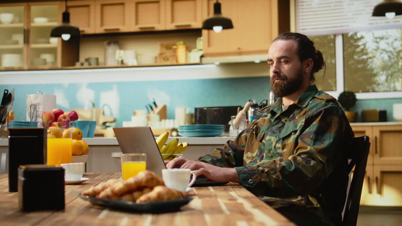 Off duty serviceman in military uniform with laptop and coffee at home
