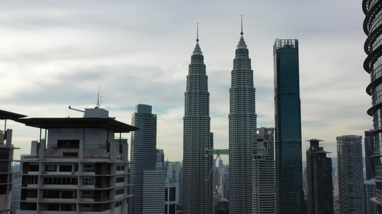 Toma Inversa de Dron Volando Entre Rascacielos de Gran Altura, Capturando las Espectaculares Torres Gemelas Petronas en el Centro de Kuala Lumpur, Malasia