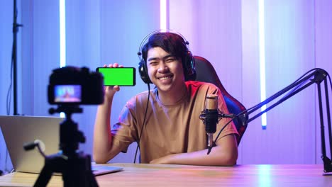 asian man holding mobile phone with mock up green screen while live stream with camera