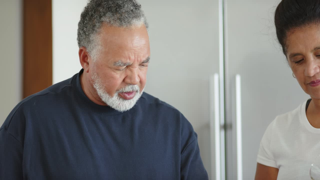 Afroamerikansk ældre par arbejder ved køkkenbordet, kvinde hælder fra kande i blender.