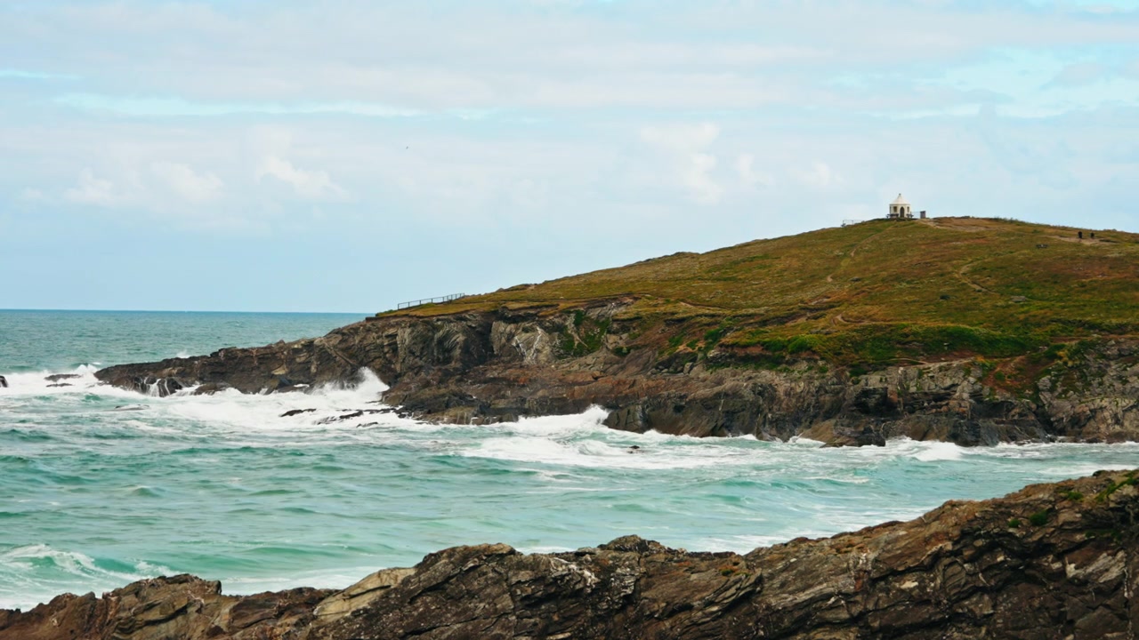 Birleşik Krallık'taki Cornwall Sahil Şeridi'nin panoramik görüntüsü. Engebeli kayalık falezler, yemyeşil tarlalar ve kayalara çarpan deniz dalgalarının manzarası. Cornwall'ı ziyaret etmek için turistik bir cazibe merkezi.